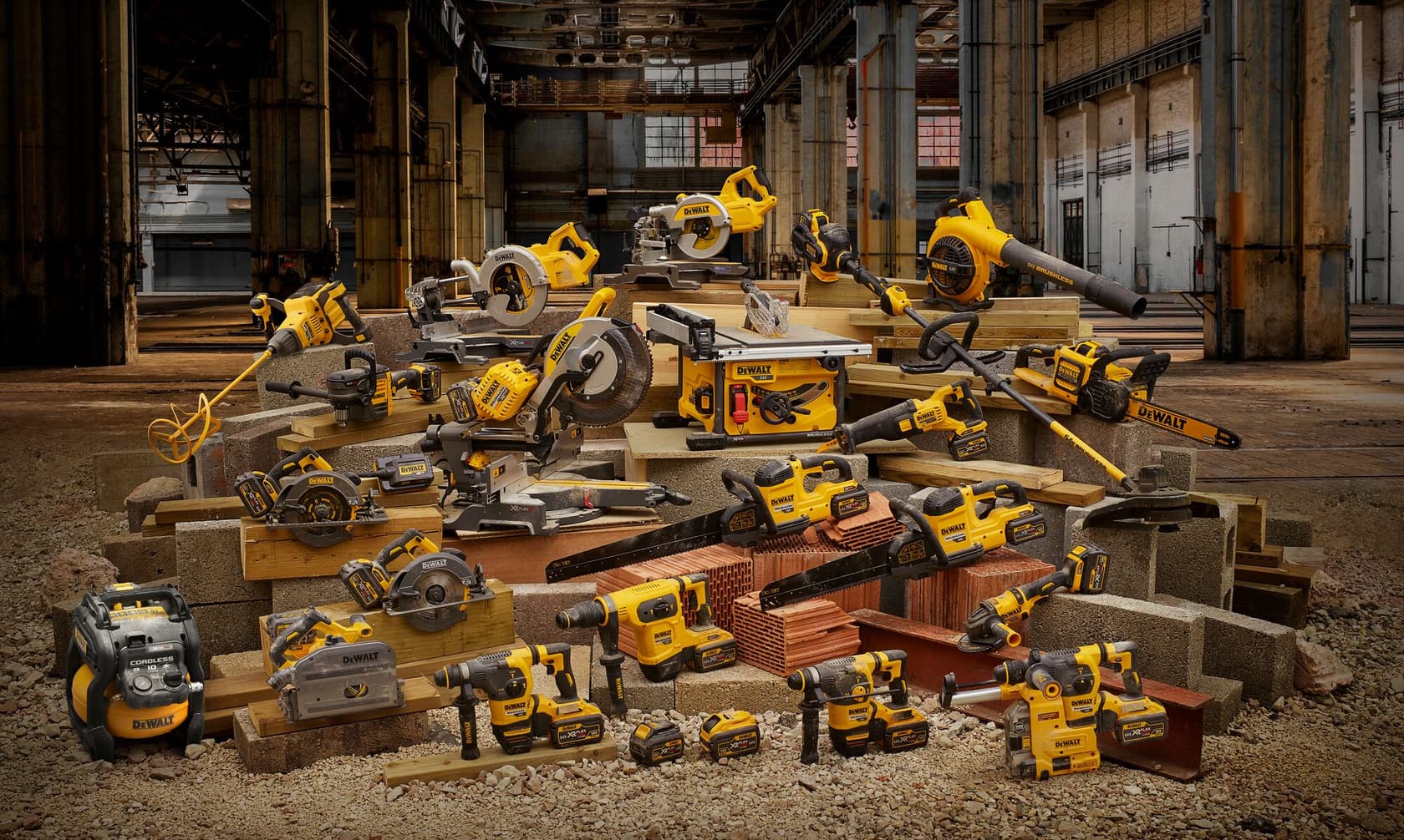 Un grupo de varias herramientas eléctricas DEWALT, incluyendo taladros, sierras, amoladoras y sopladores, dispuestas sobre materiales de construcción dentro de un edificio industrial.